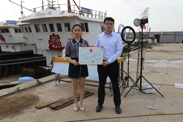 海鮮電商張夢(mèng)琴與幫辦員手持食品經(jīng)營許可證合影。贛榆區(qū)委宣傳部供圖