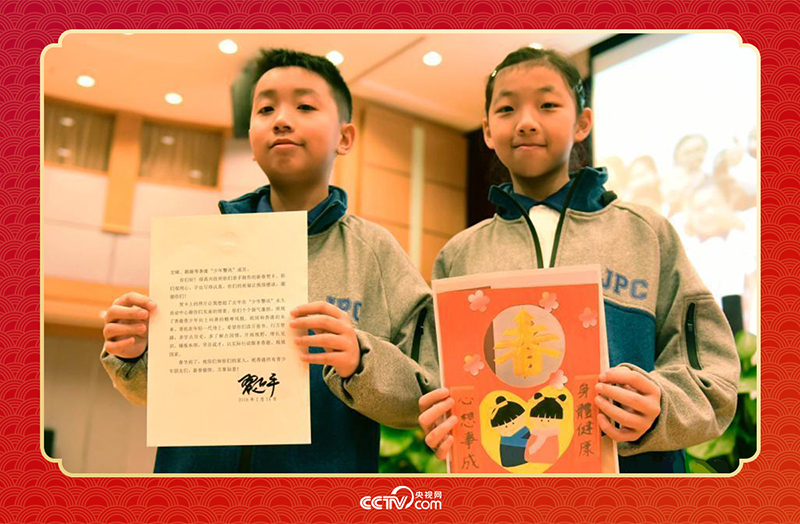 圖為香港“少年警訊”成員郭宏晞（左）展示習(xí)主席回信、羅顥凝（右）展示送給習(xí)主席的賀卡并合影。