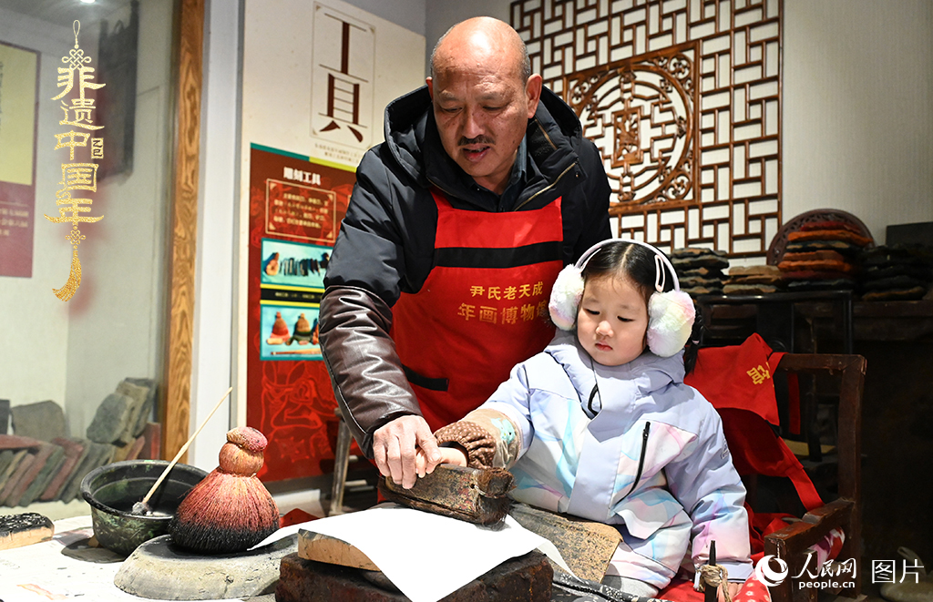 2025年1月27日，河南開封朱仙鎮(zhèn)木版年畫藝人尹國法指導(dǎo)小朋友研習(xí)年畫印制技藝。朱仙鎮(zhèn)木版年畫源自漢唐壁畫藝術(shù)，是中國木版年畫的鼻祖。2006年5月20日，朱仙鎮(zhèn)木版年畫經(jīng)國務(wù)院批準列入第一批國家級非物質(zhì)文化遺產(chǎn)名錄。人民網(wǎng)記者 王玉興攝